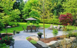home patio with trees, shrubs and flowers near table, chairs and umbrella