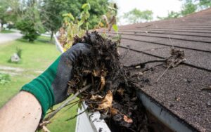 Hand pulling debris from a home's gutter